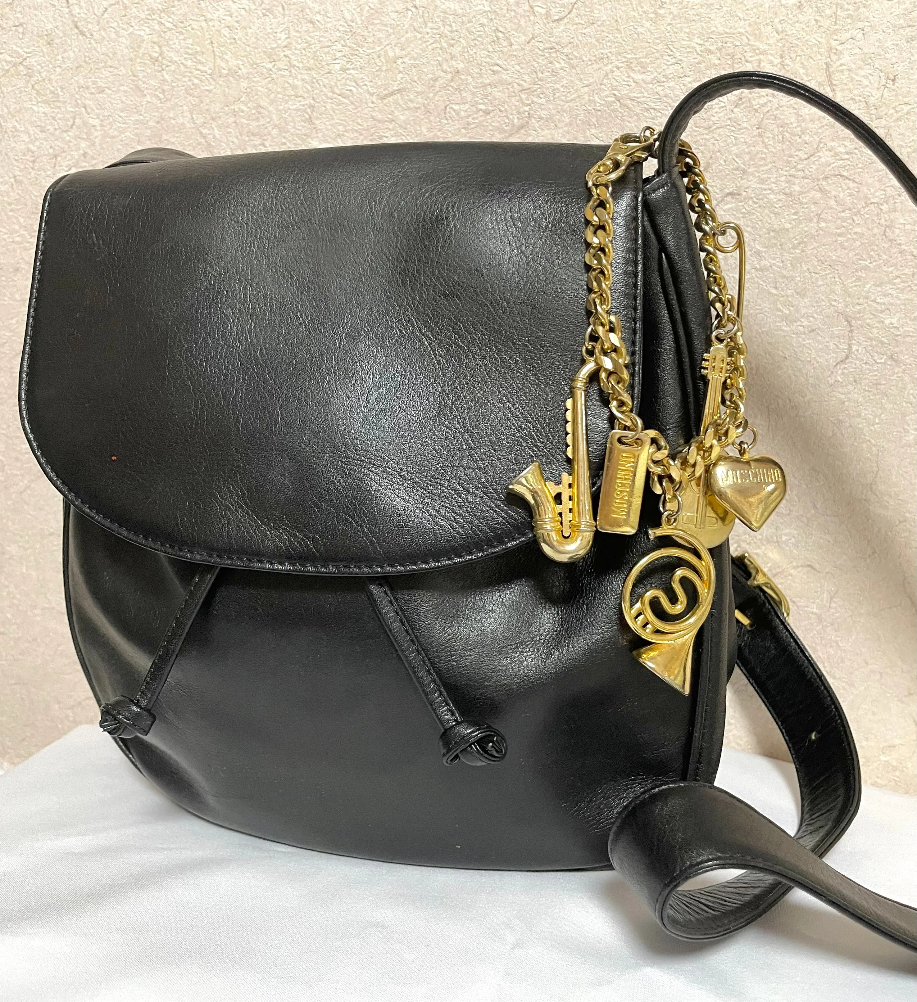 Vintage Moschino black leather shoulder bag with golden cute dangling charms. Heart, safety pin, trumpet, sacks, and guitar. 050725