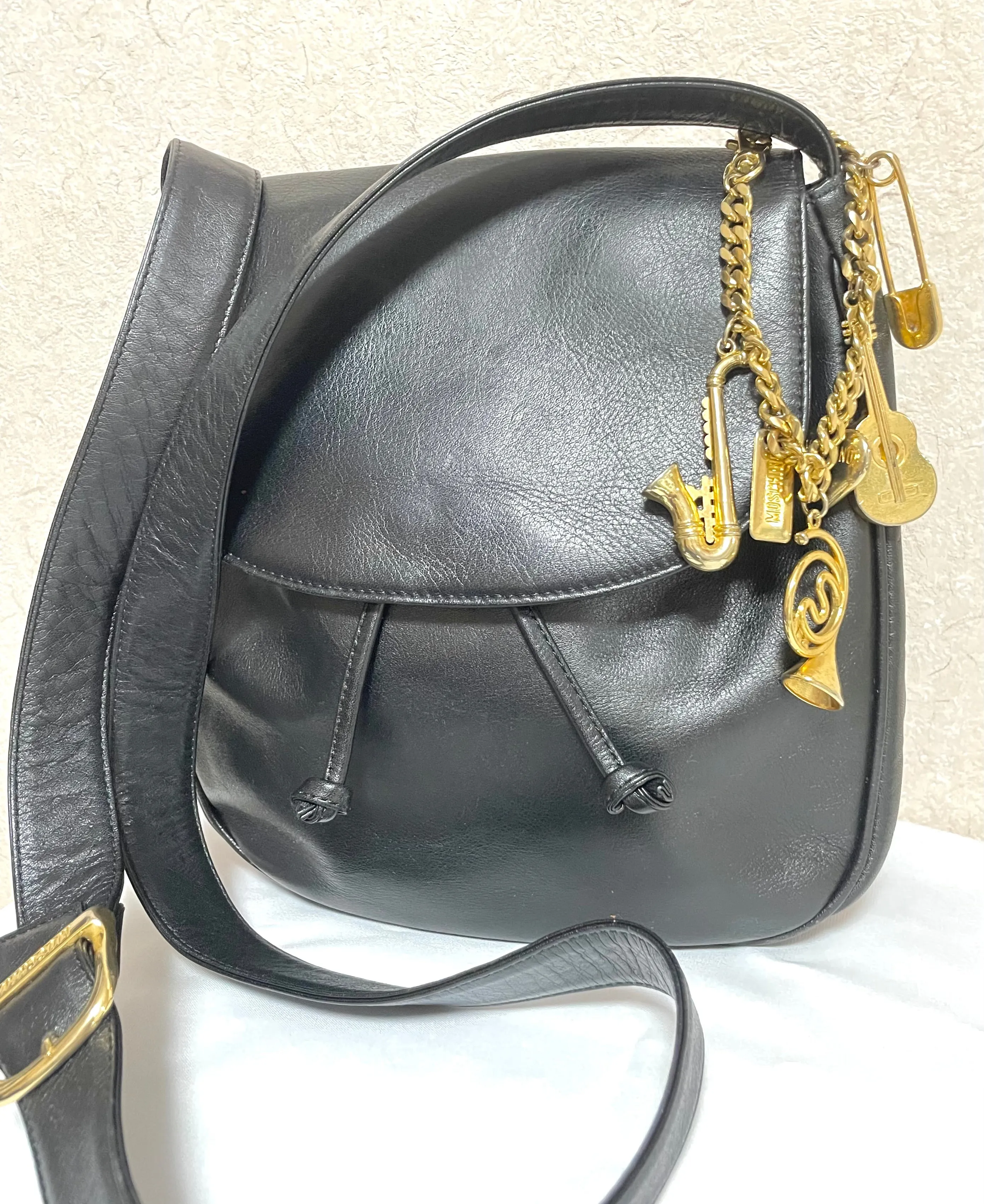Vintage Moschino black leather shoulder bag with golden cute dangling charms. Heart, safety pin, trumpet, sacks, and guitar. 050725