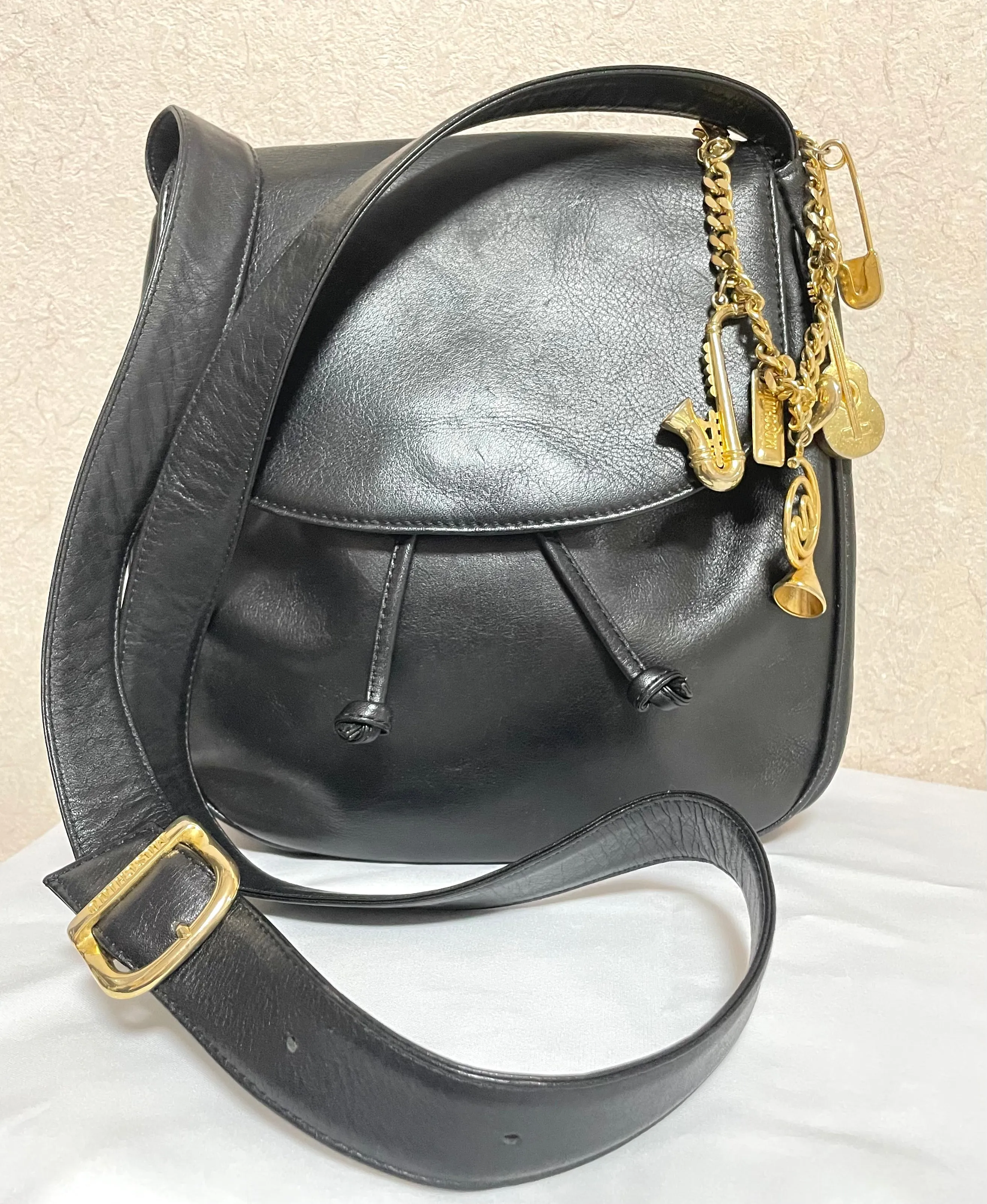 Vintage Moschino black leather shoulder bag with golden cute dangling charms. Heart, safety pin, trumpet, sacks, and guitar. 050725