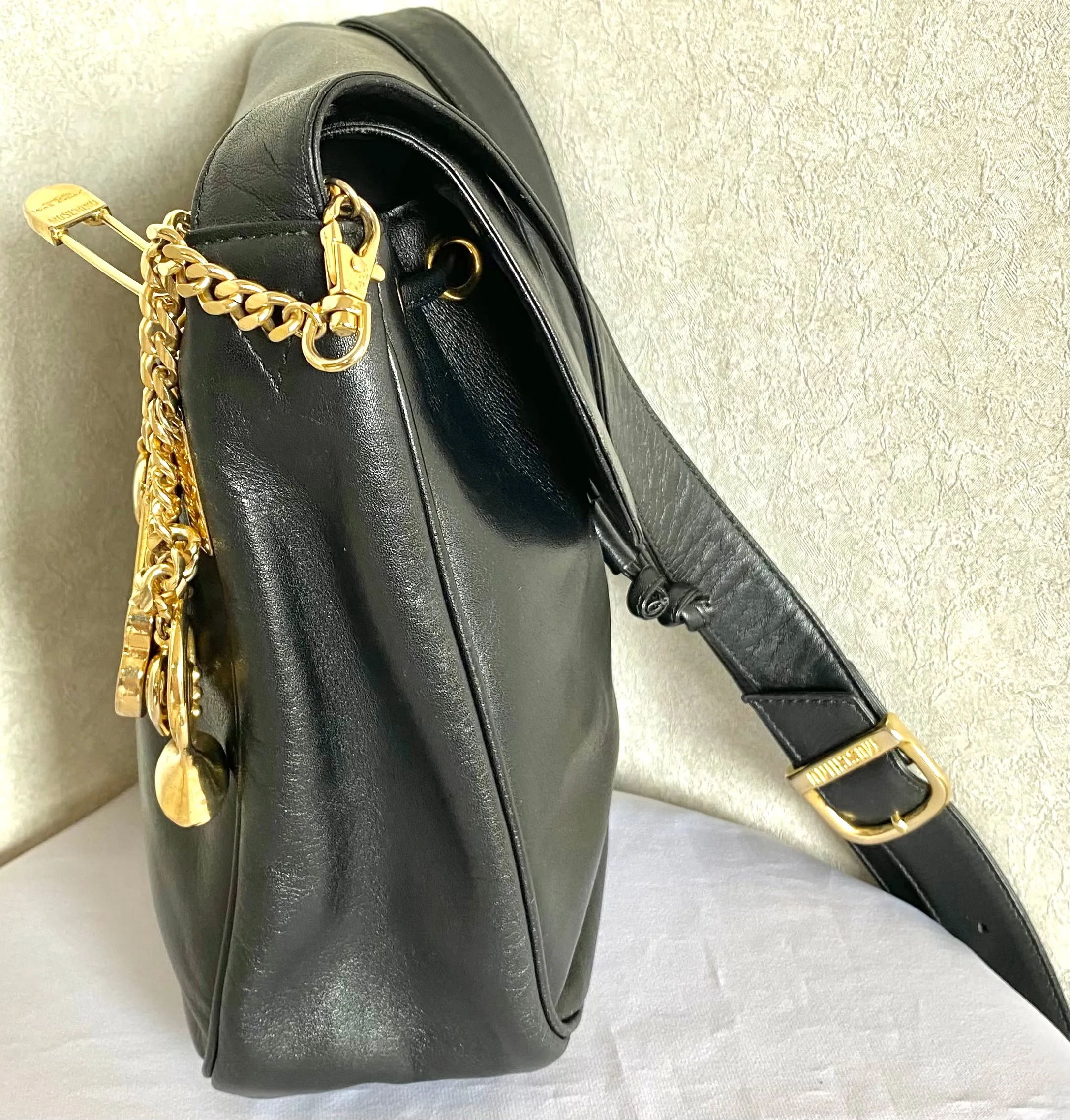 Vintage Moschino black leather shoulder bag with golden cute dangling charms. Heart, safety pin, trumpet, sacks, and guitar. 050725