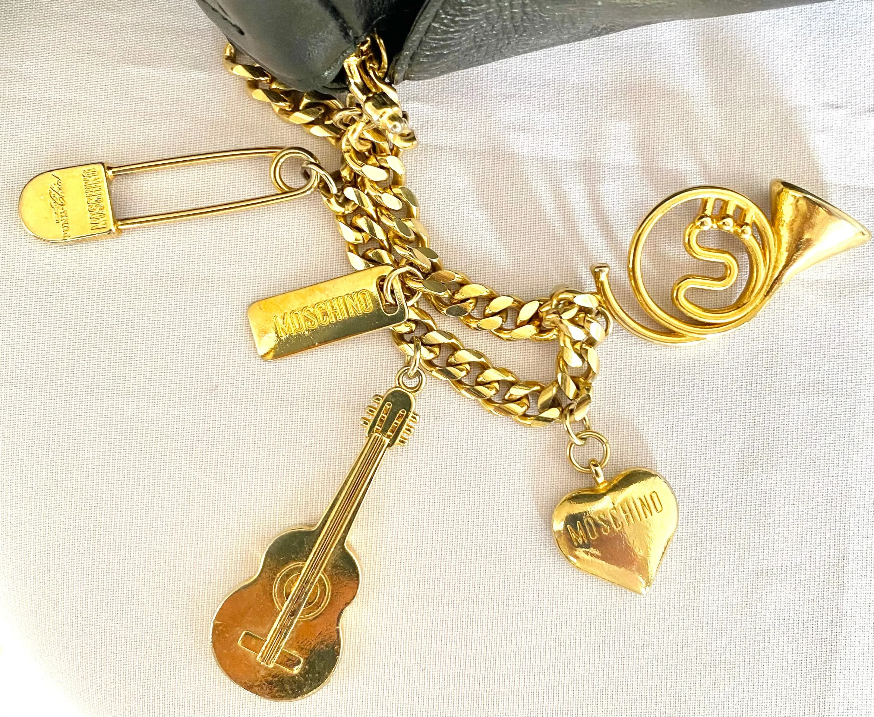 Vintage Moschino black leather shoulder bag with golden cute dangling charms. Heart, safety pin, trumpet, sacks, and guitar. 050725